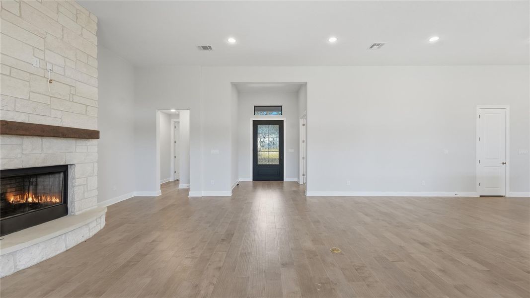 Unfurnished living room with light wood-style flooring, a stone fireplace, and recessed lighting Unfurnished living room with light wood-style flooring, a stone fireplace, and recessed lighting