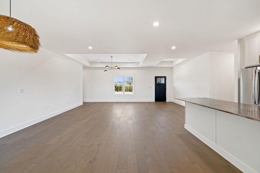 Unfurnished living room featuring a raised ceiling, dark wood-style floors, and hanging lights