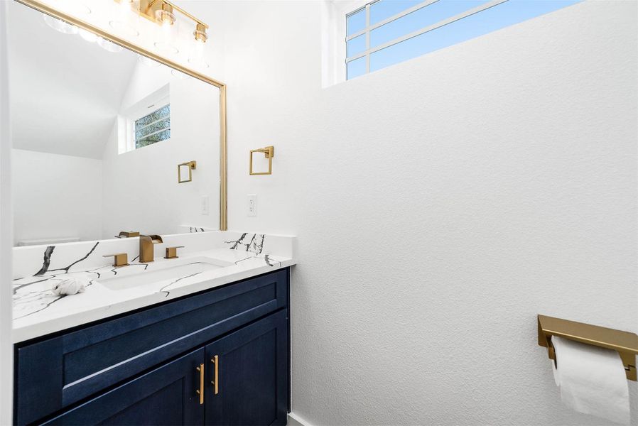 Stylish half bath featuring a quartz vanity, ash blue cabinetry, and elegant gold fixtures.