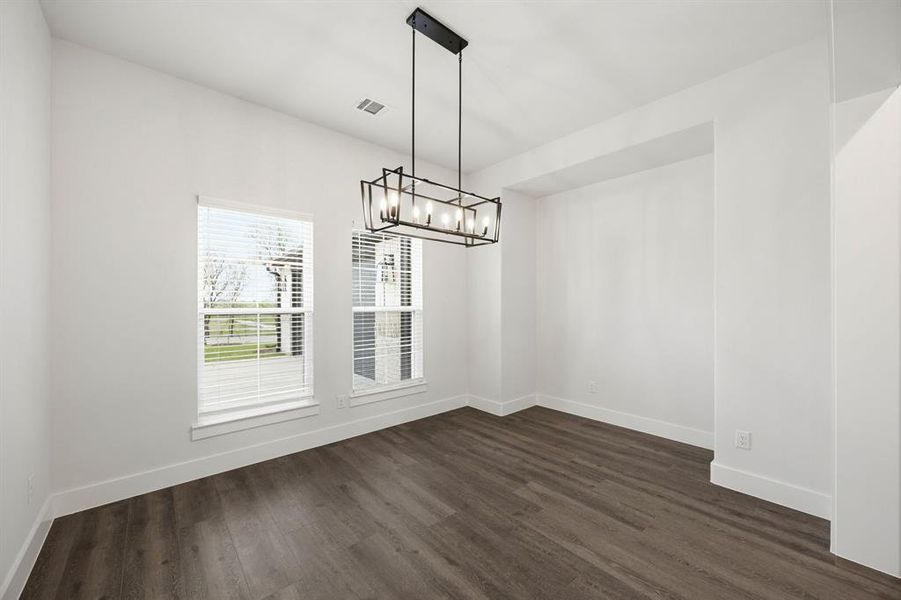 Spacious interior room featuring wood-finish flooring, white baseboards, and a contemporary linear chandelier
