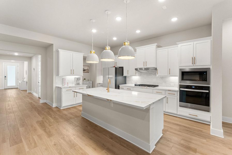 The island kitchen has Silestone counters, 42” Shaker style cabinets with gold hardware, pendant lights, breakfast bar, tile backsplash and walk-in pantry. The stainless steel appliances include a five-burner cooktop, oven, microwave, dishwasher, and vent hood.