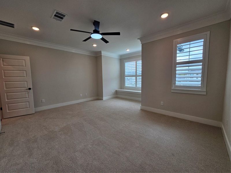 This spacious, carpeted room features neutral walls, recessed lighting, a modern ceiling fan, and two large windows with plantation shutters, offering ample natural light.
