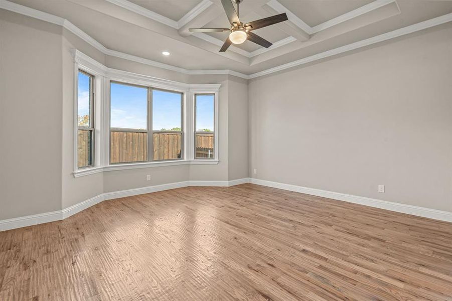 Empty room featuring light wood-type flooring, crown molding, coffered ceiling, ceiling fan, and beamed ceiling Empty room featuring light wood-type flooring, crown molding, coffered ceiling, ceiling fan, and beamed ceiling