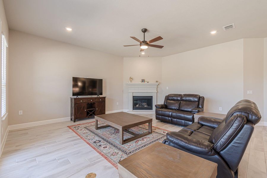 Living area featuring light wood finished floors, recessed lighting, visible vents, a glass covered fireplace, and baseboards