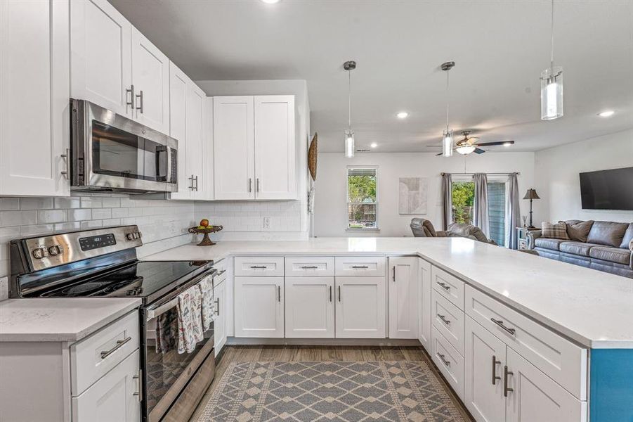 Kitchen featuring appliances with stainless steel finishes, open floor plan, pendant lighting, white cabinets, and recessed lighting