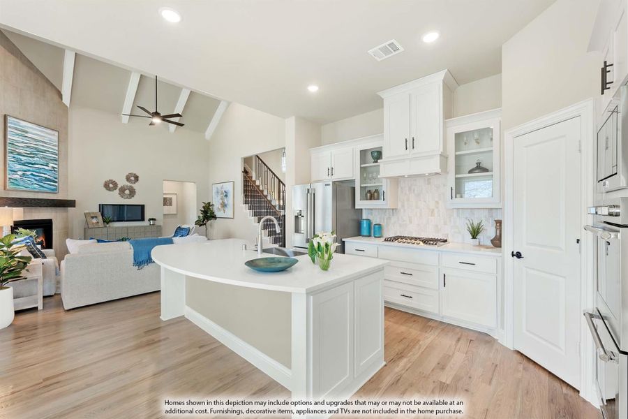 Open-concept kitchen with white cabinets, curved island, and hardwood floors, open to living room with fireplace and vaulted ceiling. Open-concept kitchen with white cabinets, curved island, and hardwood floors, open to living room with fireplace and vaulted ceiling.