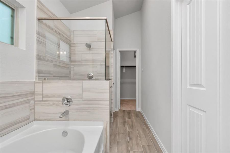 Step into the sleek and modern primary bathroom featuring a luxurious combination of tile and glass elements. The walk-in shower with a glass enclosure and stylish, light-colored tiles adds a touch of elegance, complemented by a relaxing bathtub. The space is bright and inviting, thanks to the clean white walls and natural light filtering in through a small window. **This image is from another Saratoga Home - Wren floorplan.**