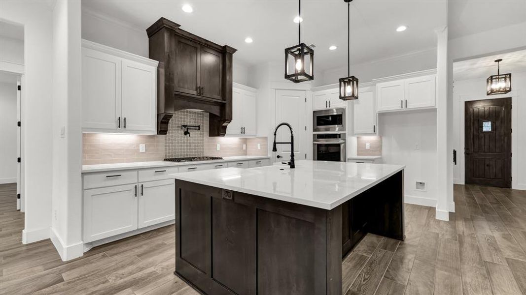 Kitchen featuring backsplash, stainless steel appliances, light hardwood / wood-style floors, and a kitchen island with sink