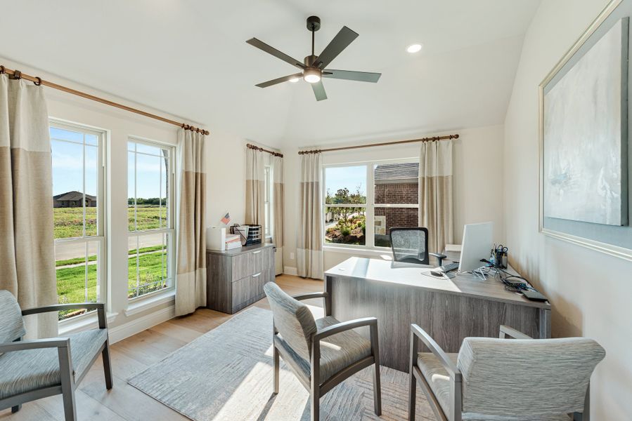 Home office with large windows, ceiling fan, wood desk, and light hardwood floors