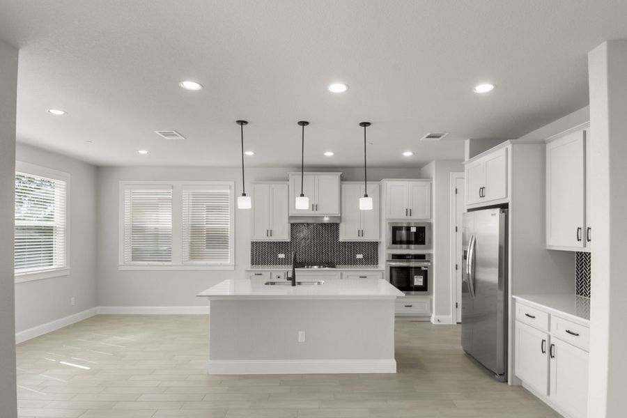 Kitchen interior with grey cabinets and white countertops with black backsplash tile and steel appliances.