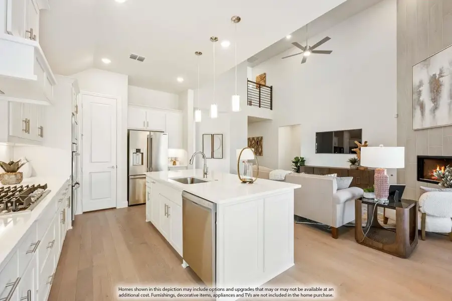 Open-concept kitchen with white island, pendant lights, and adjoining living room with fireplace and high ceilings