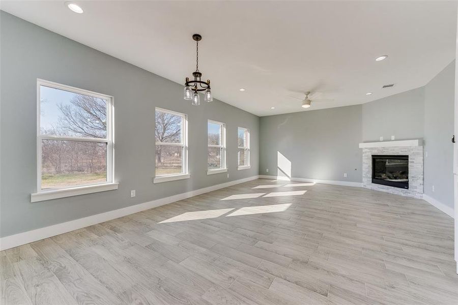 Unfurnished living room featuring a stone fireplace, light hardwood / wood-style flooring, and ceiling fan with notable chandelier