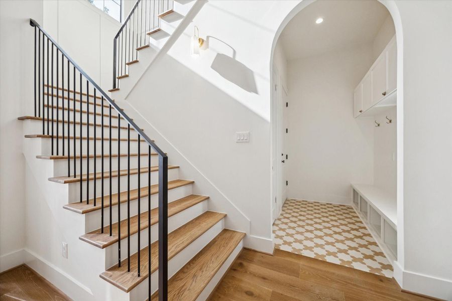 Bright entry with a wood staircase, sleek iron railing, arched hallway, and built-in mudroom storage.