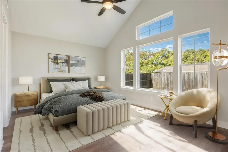 Virtually staged primary bedroom with high vaulted ceiling, wood finished floors, and a ceiling fan