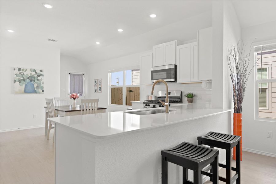 Gleaming stone countertops and pristine white cabinetry define this chef-inspired kitchen, which opens seamlessly to a sunlit dining nook perfect for morning gatherings.