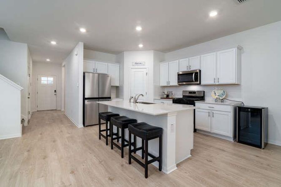 Kitchen featuring appliances with stainless steel finishes, a kitchen bar, an island with sink, light wood-style flooring, and recessed lighting