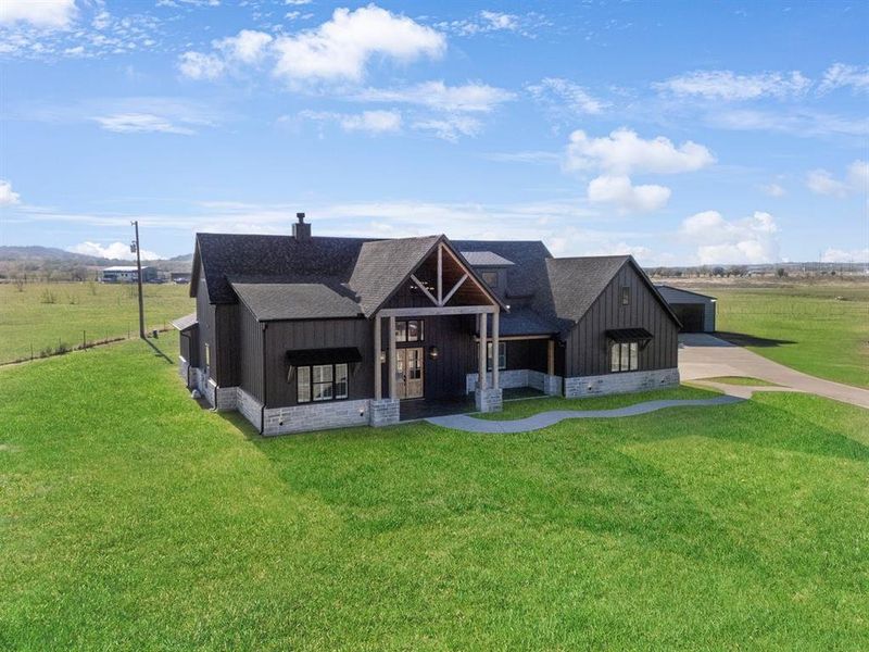 Modern farmhouse with board and batten siding, roof with shingles, covered porch, and a front yard