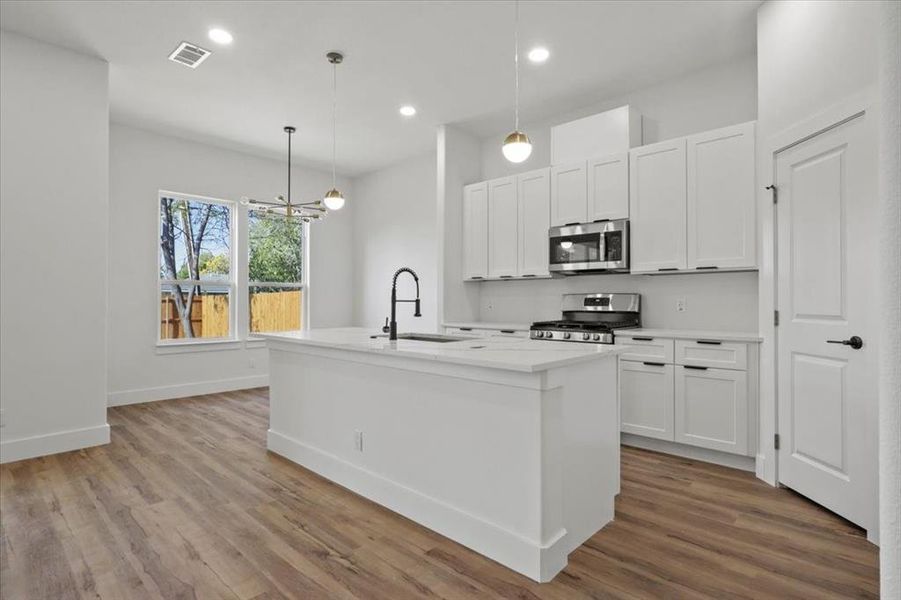 Kitchen with a center island with sink, pendant lighting, white cabinetry, stainless steel appliances, and recessed lighting