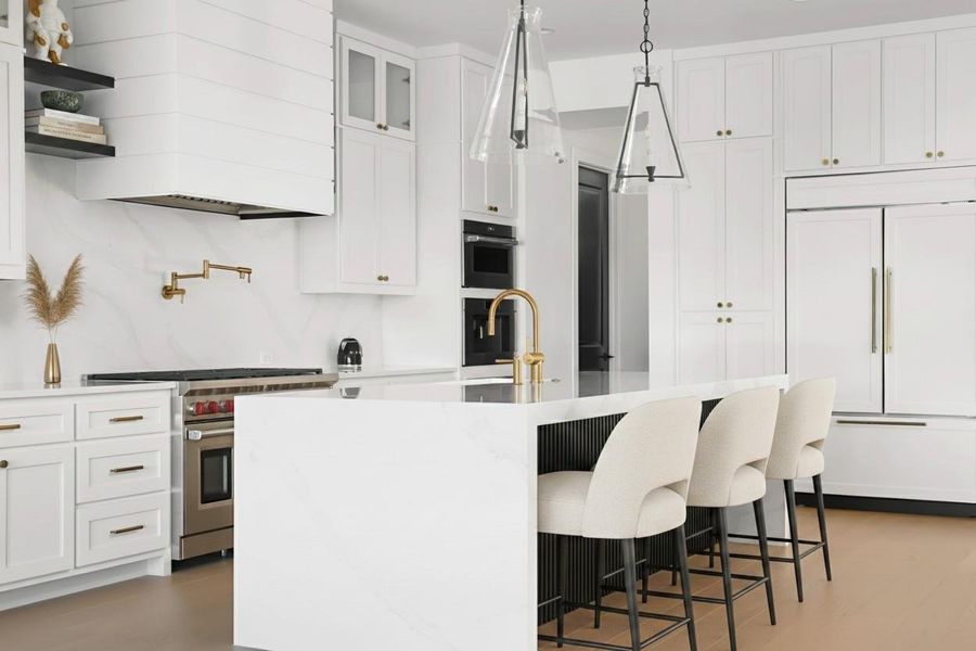 Contemporary kitchen featuring a large central island, white cabinetry, integrated appliances, and a gold-finish pot filler