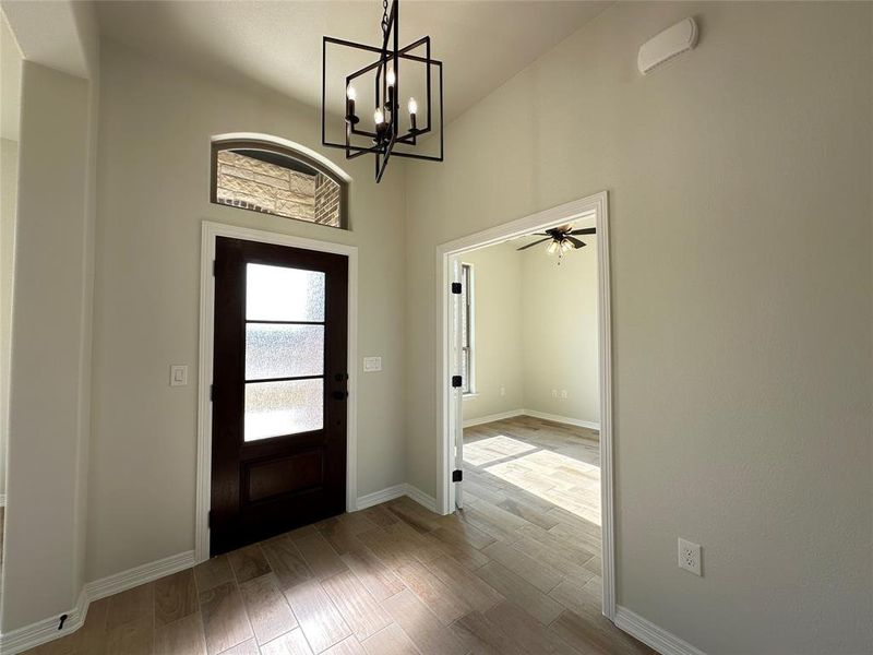 Foyer entrance featuring wood tiled floors, a ceiling fan, a towering ceiling, and a chandelier