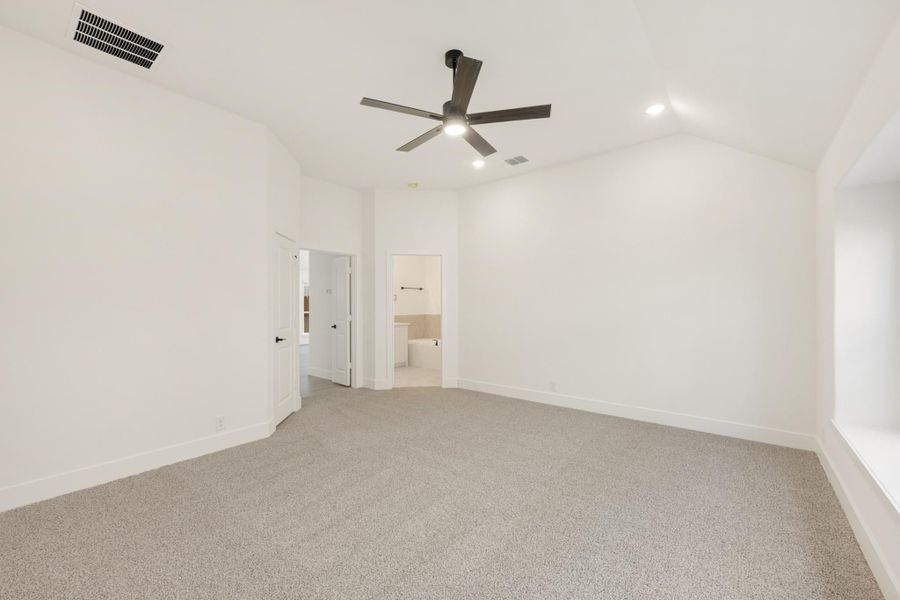 Empty bedroom with vaulted ceiling, ceiling fan, gray carpet, and ensuite bathroom doorway Empty bedroom with vaulted ceiling, ceiling fan, gray carpet, and ensuite bathroom doorway
