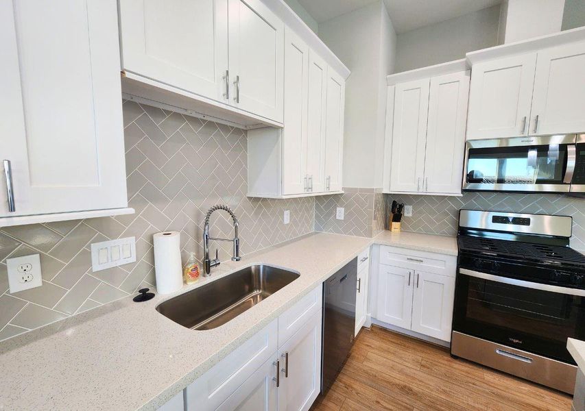 This modern kitchen features sleek white cabinetry, a stylish herringbone tile backsplash, and stainless steel appliances. The spacious countertop and undermount sink add functionality and elegance. This modern kitchen features sleek white cabinetry, a stylish herringbone tile backsplash, and stainless steel appliances. The spacious countertop and undermount sink add functionality and elegance.