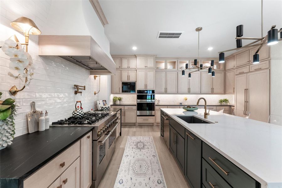 The kitchen features a professional layout with a large island, honed black granite perimeter counters, and upgraded appliance selections. A custom hood and statement backsplash create a tailored designer focal point.