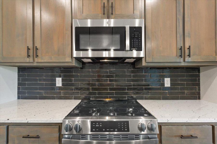 Kitchen with stainless steel appliances, light stone countertops, and tasteful backsplash