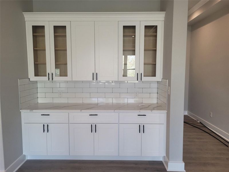 Bar area featuring white cabinets, light stone counters, decorative backsplash, and dark wood finished floors