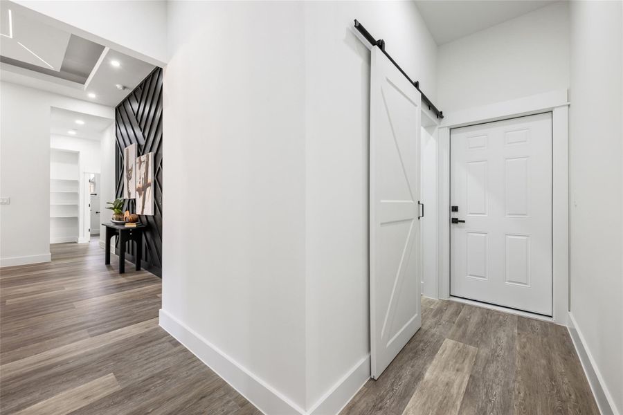 Wood-finish flooring throughout, featuring a modern accent wall with geometric paneling, recessed lighting, and a white barn door