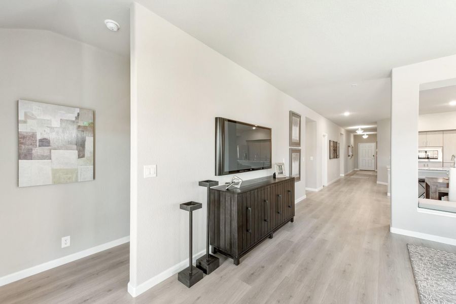 Open hallway with light wood floors, wall-mounted TV, dark wood console table, and view to kitchen Open hallway with light wood floors, wall-mounted TV, dark wood console table, and view to kitchen