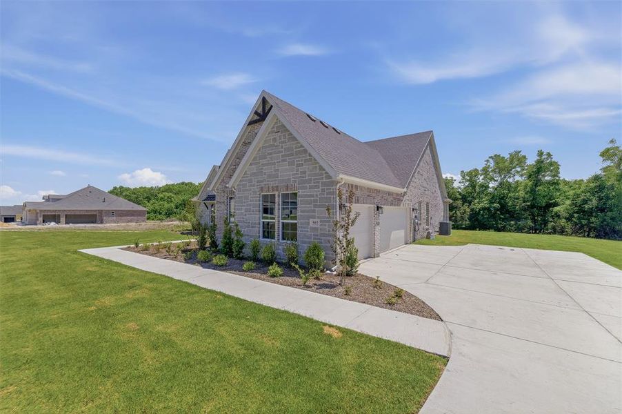 Stone facade home featuring a two-car garage, concrete driveway, and manicured lawn