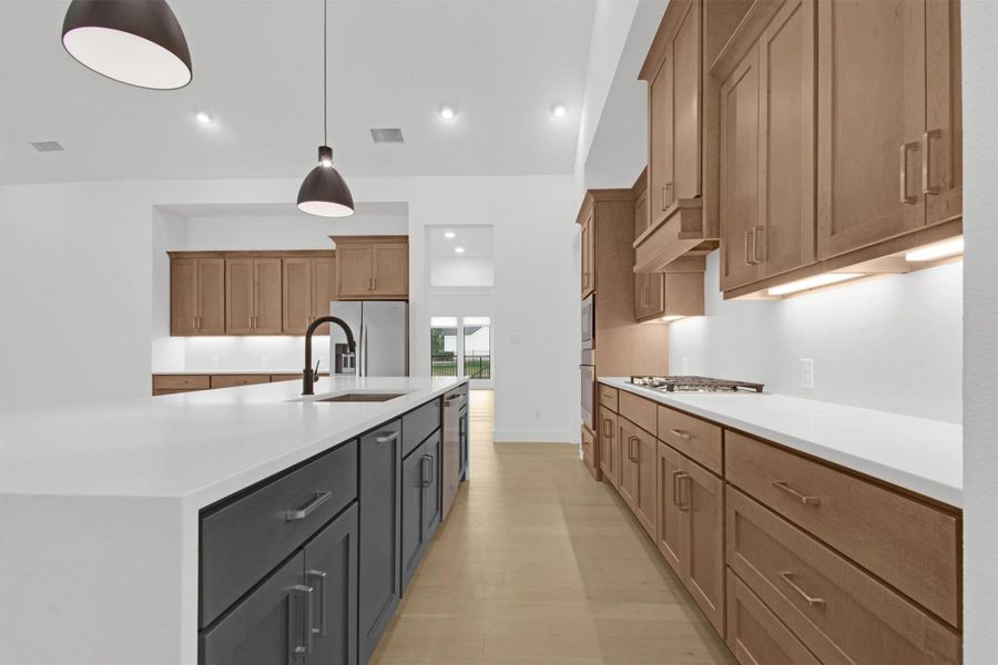 Kitchen featuring wood cabinets, a spacious island, quartz countertops, hanging light fixtures, stainless steel appliances, and light hardwood floors