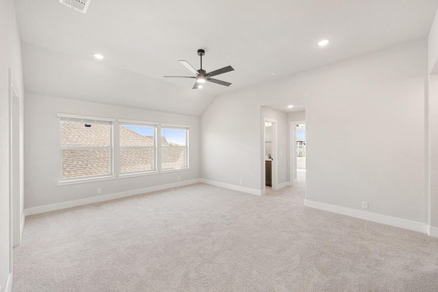 Spacious bedroom with vaulted ceiling, ceiling fan, carpet flooring, and doorway to ensuite bathroom Spacious bedroom with vaulted ceiling, ceiling fan, carpet flooring, and doorway to ensuite bathroom