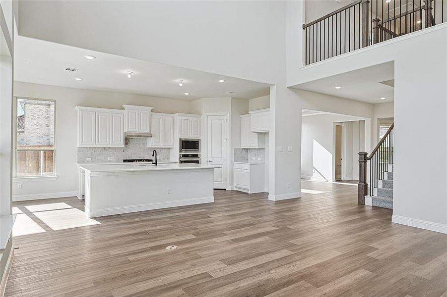 Kitchen with a kitchen island with sink, decorative backsplash, light wood-type flooring, white cabinetry, and stainless steel appliances