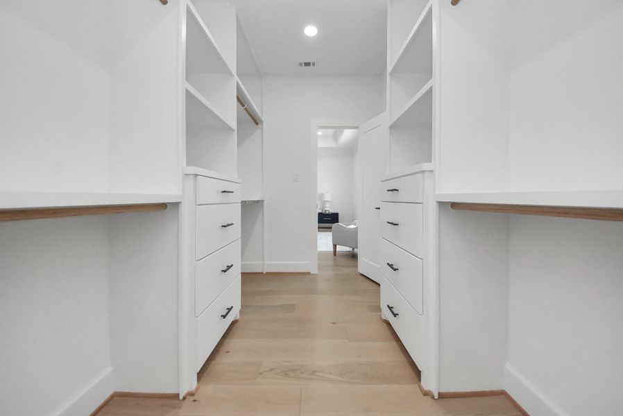 Step into this expansive walk-in closet, featuring ample shelving, drawers, and hanging space. Light wood flooring and white cabinetry create a bright, modern environment, offering plenty of storage and organization for everyday living. Step into this expansive walk-in closet, featuring ample shelving, drawers, and hanging space. Light wood flooring and white cabinetry create a bright, modern environment, offering plenty of storage and organization for everyday living.
