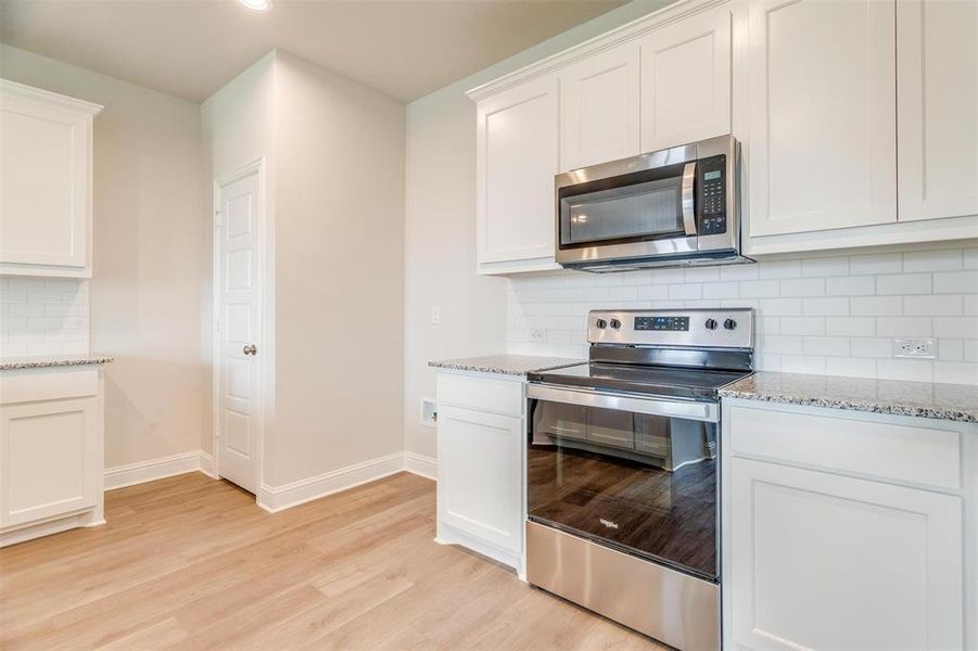 Kitchen with white cabinetry, tasteful backsplash, light hardwood / wood-style flooring, stainless steel appliances, and light stone countertops