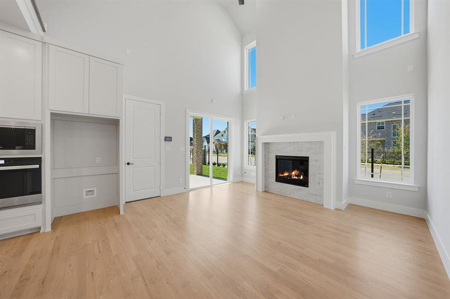 Unfurnished living room with light wood-style flooring, a glass covered fireplace, and a high ceiling