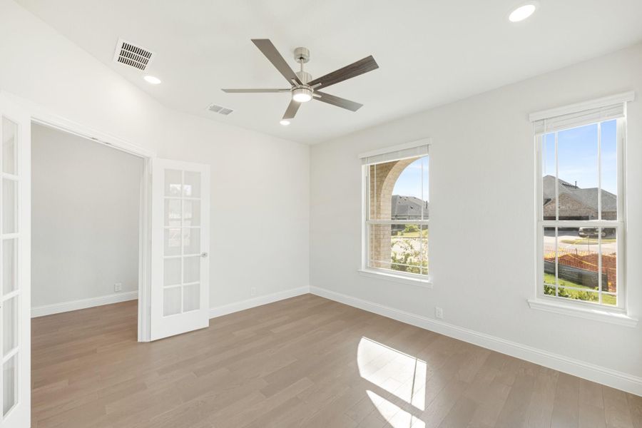 Empty room with hardwood floors, ceiling fan, two windows, and French doors leading to adjacent space