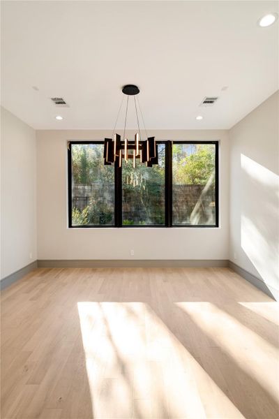 This room features a modern chandelier, large windows with garden views, and light wood flooring. It's bright and airy, offering a serene atmosphere ideal for dining or relaxation.