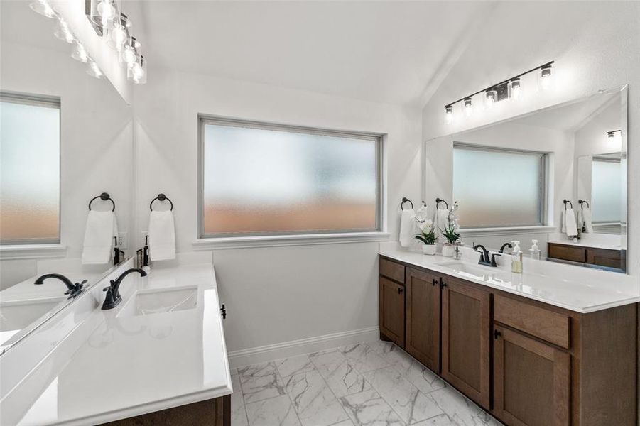 Bathroom with two vanities, lofted ceiling, and light marble finish floors