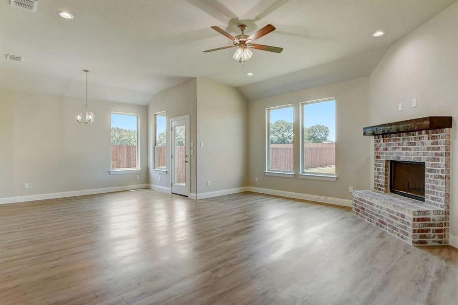 Unfurnished living room with plenty of natural light, lofted ceiling, a brick fireplace, wood finished floors, and baseboards