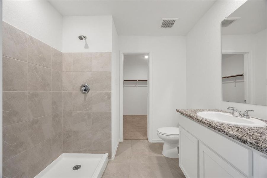 Full bathroom featuring a walk-in shower with light-toned wall tile, a white vanity cabinet, a speckled countertop, a single basin sink, and an integrated mirror