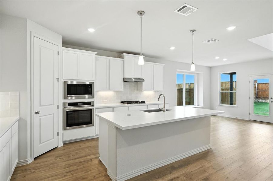 Kitchen featuring decorative backsplash, white cabinets, stainless steel appliances, hanging light fixtures, and recessed lighting