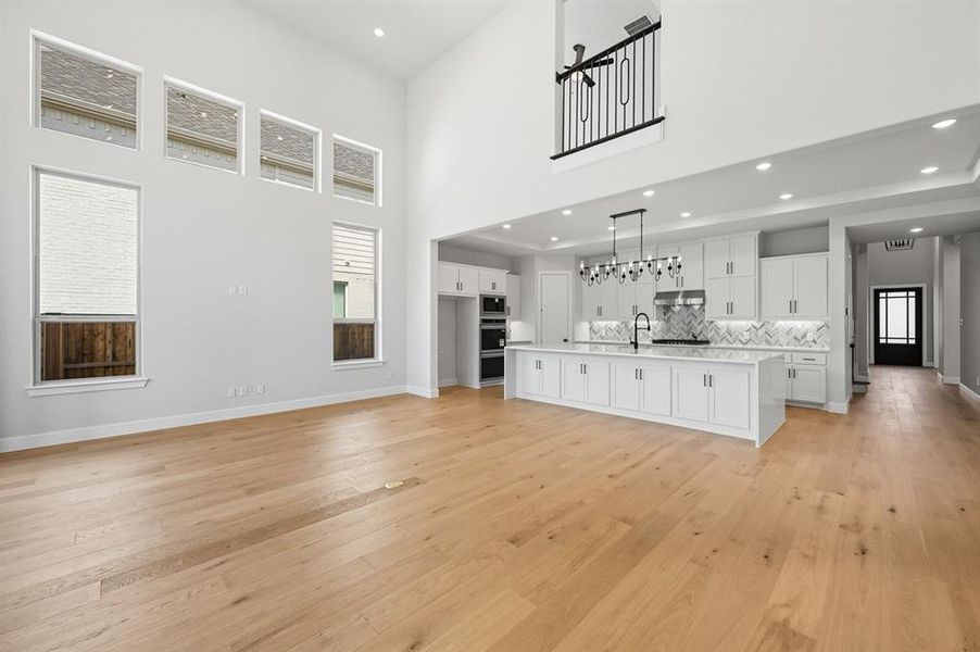 Unfurnished living room featuring recessed lighting, light wood finished floors, and a towering ceiling
