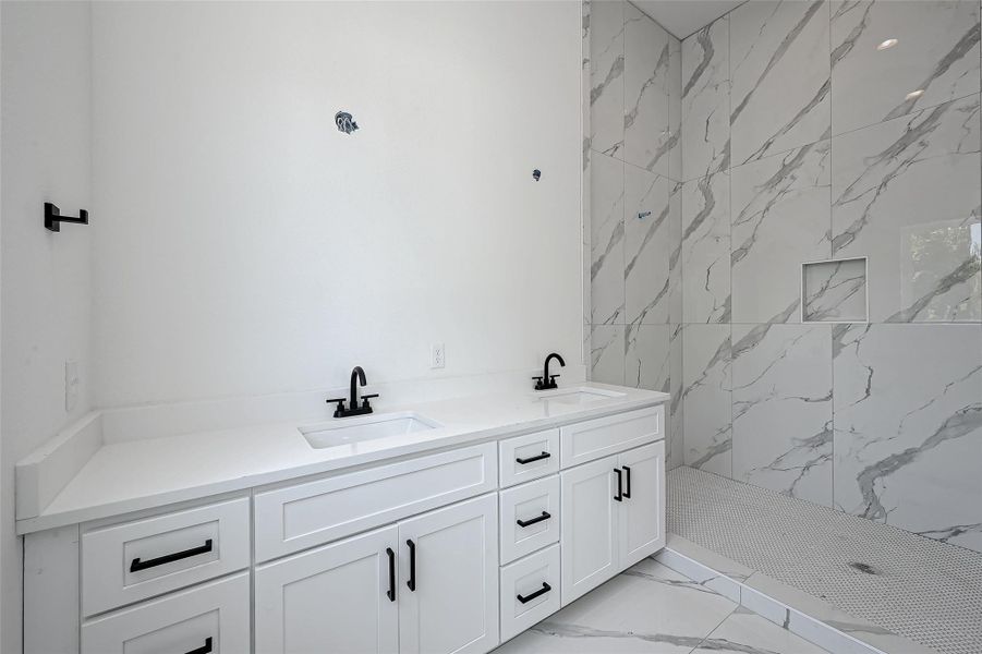 Step into luxury with this double vanity bath featuring matte black hardware, quartz countertops, and a spa-like walk-in shower clad in oversized marble-look tile with built-in niche.