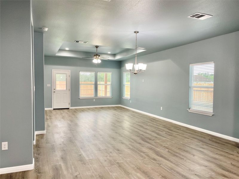 An airy living area offers ample space for entertaining with light wood-look flooring and a tray ceiling.