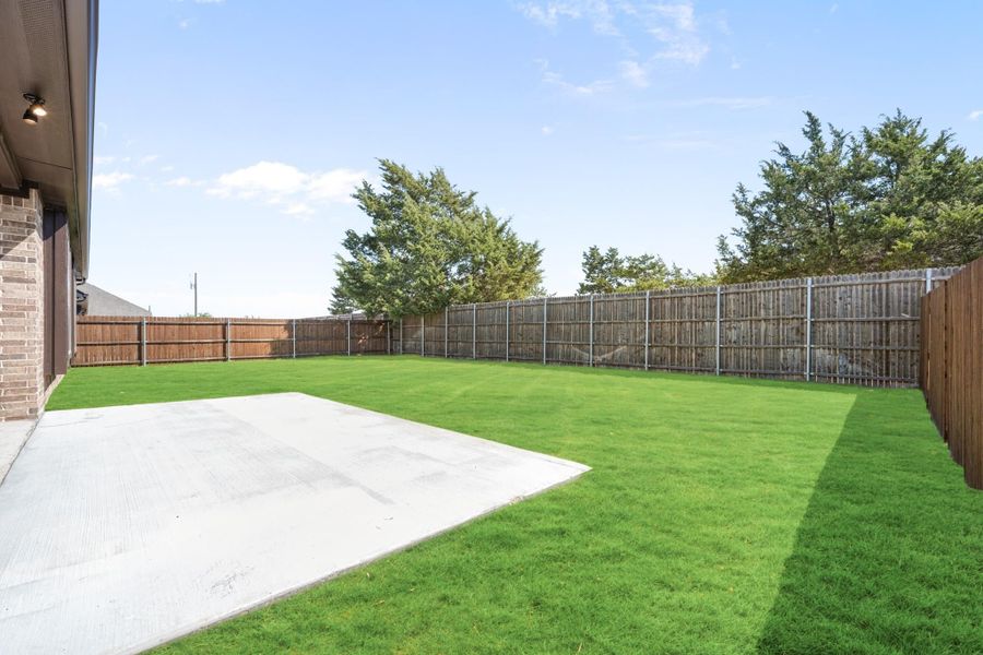 Backyard with green lawn, concrete patio, and tall wooden privacy fence surrounding the yard