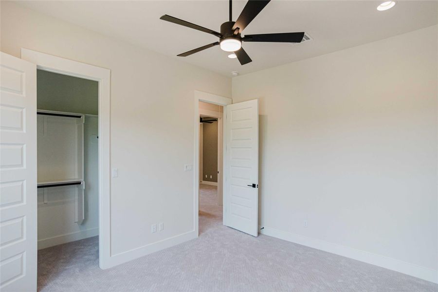 Unfurnished bedroom featuring a spacious closet, light colored carpet, and a ceiling fan