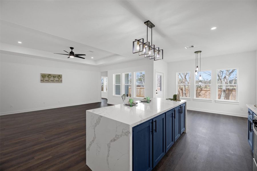 Striking blue cabinetry and elegant pendant lighting, opening to a bright space with large windows and a ceiling fan.
